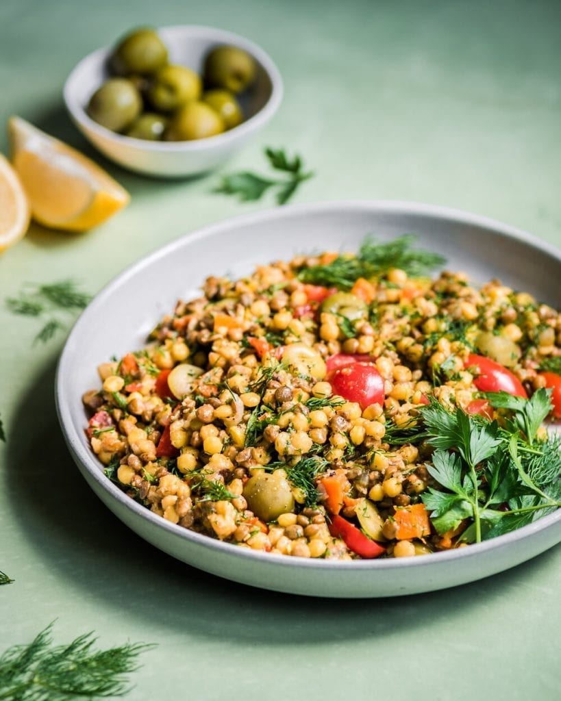 bowl of pearl couscous and lentil salad with tomatoes, parsley, and olive