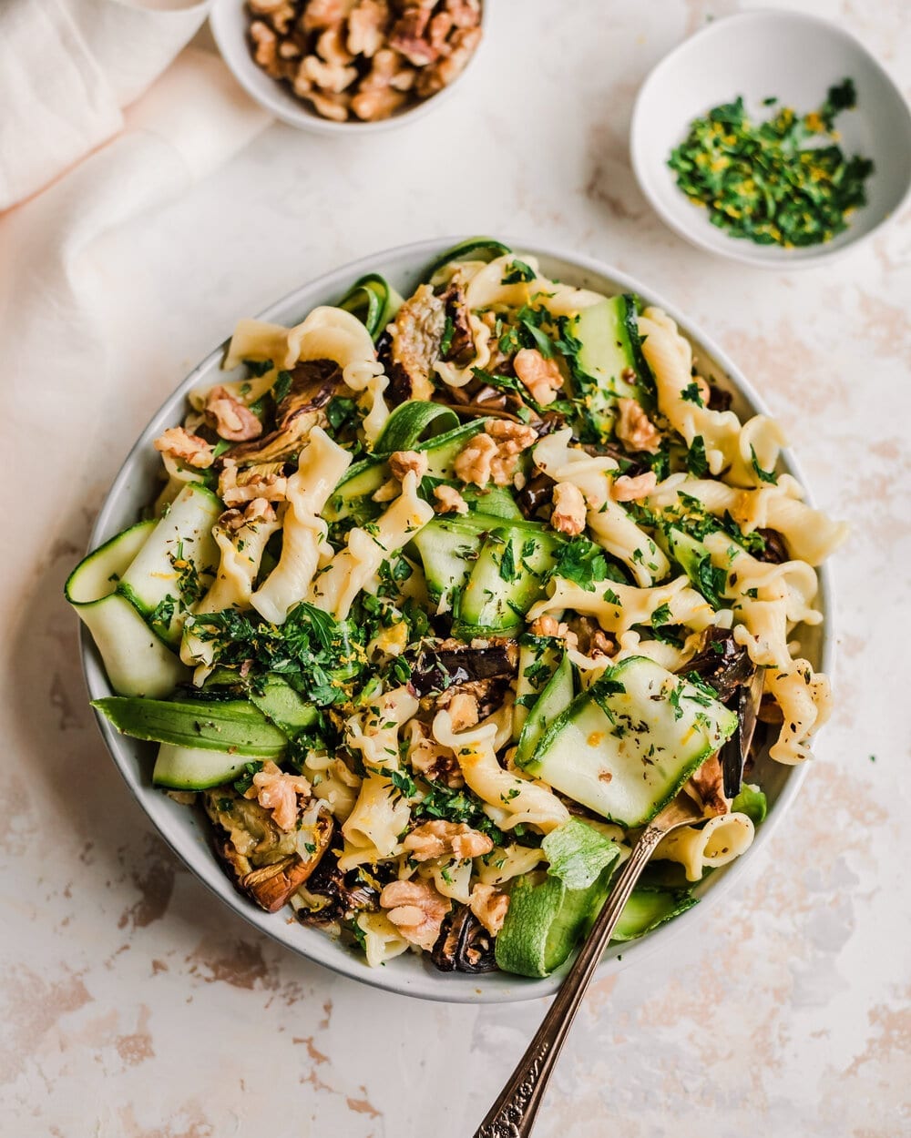 roasted eggplant pasta with zucchini ribbons and walnuts on light pink surface. 