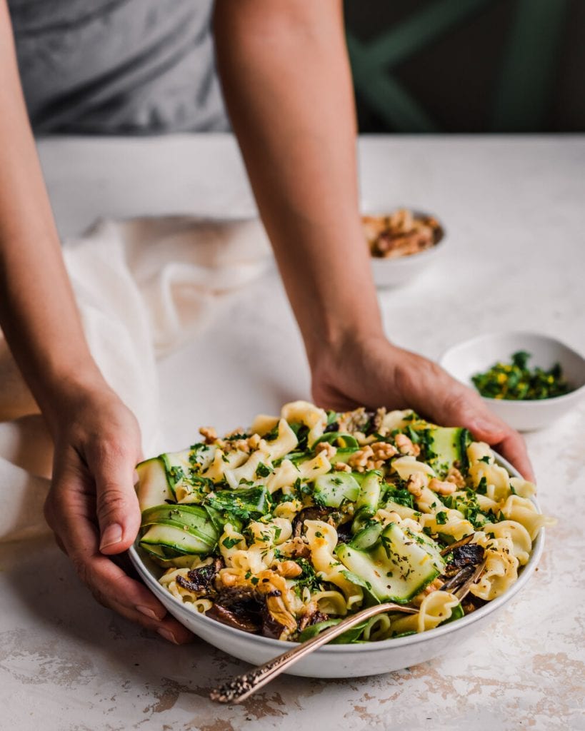 woman's hands putting down a bowl of roasted eggplant pasta on the table.