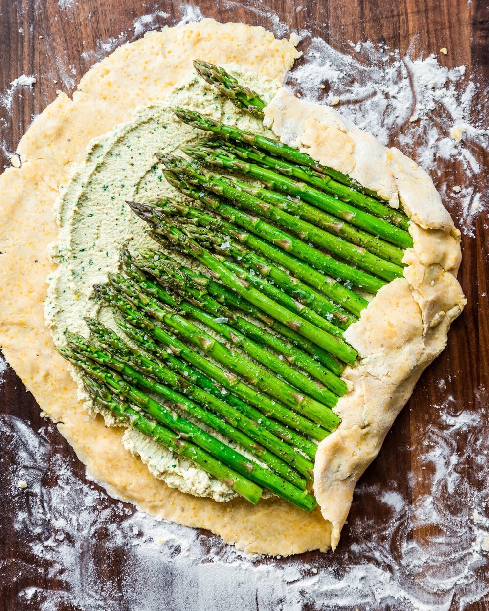 Dough underneath and folded over two sides of the asparagus and tofu ricotta on a wooden cutting board.