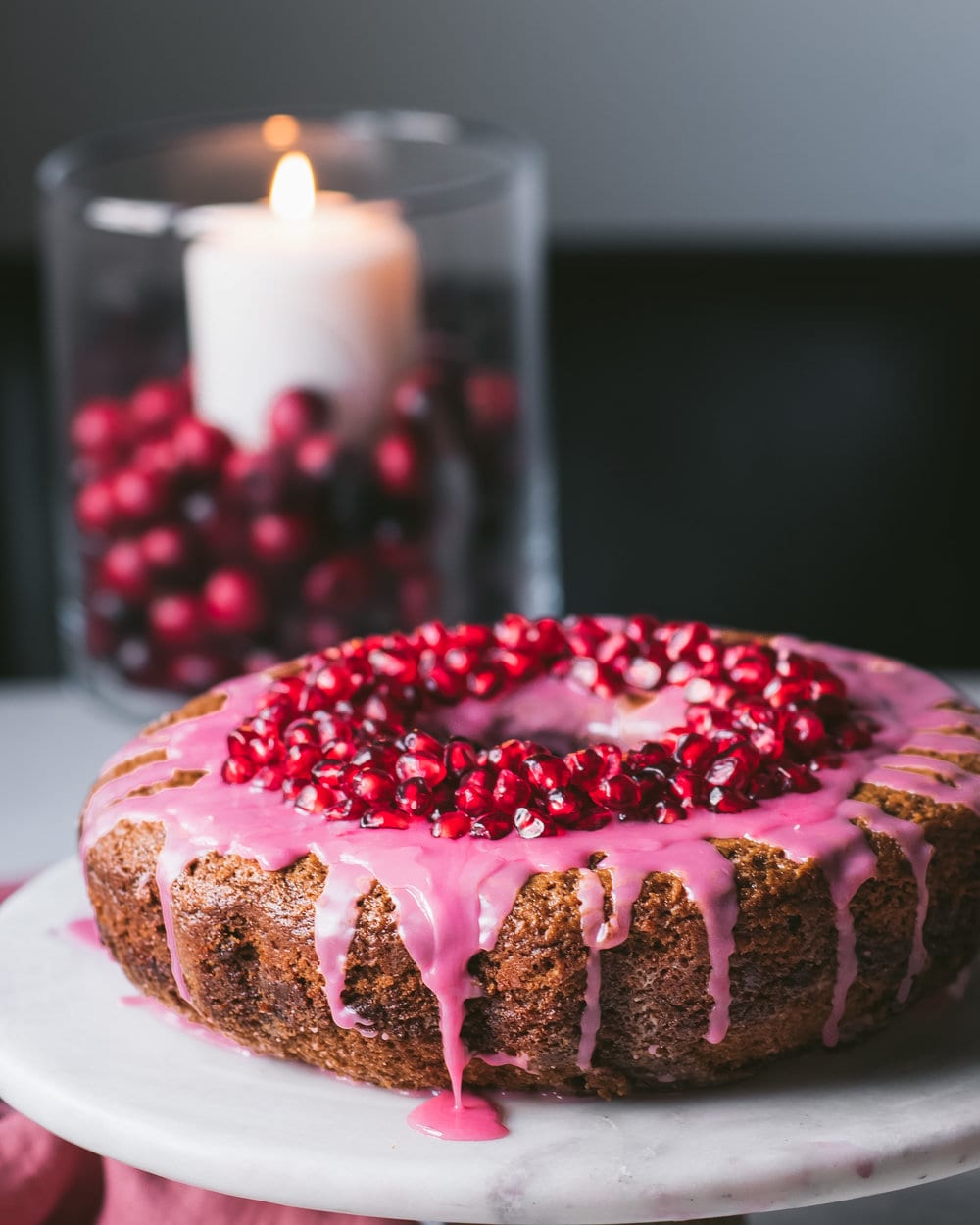 Finished pomegranate cake with pomegranate perils and icing sitting on a white cake stand.