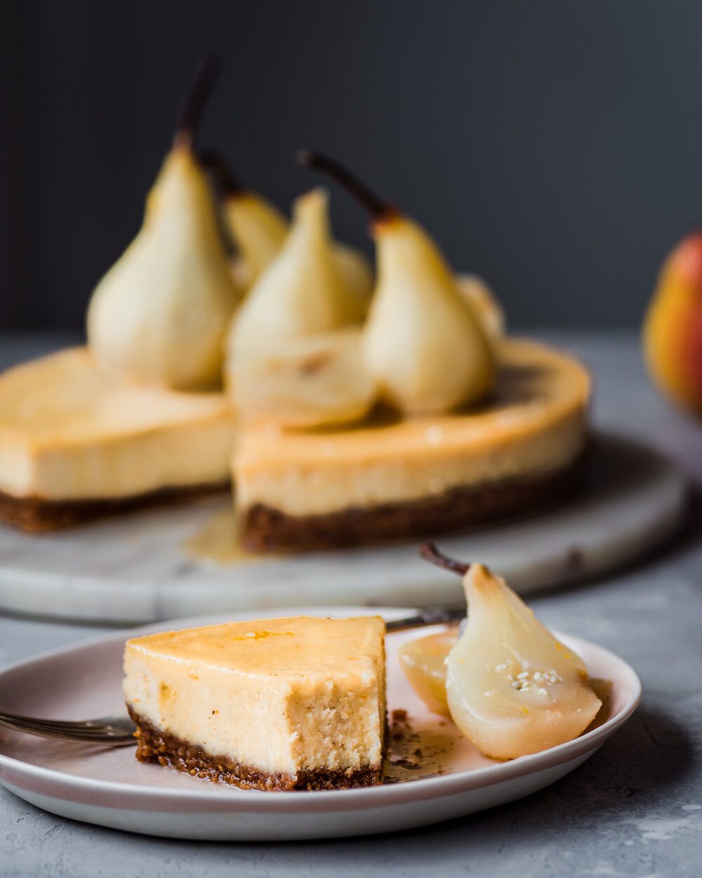 Piece of cheesecake and two poached pear halves on a plate with a fork.