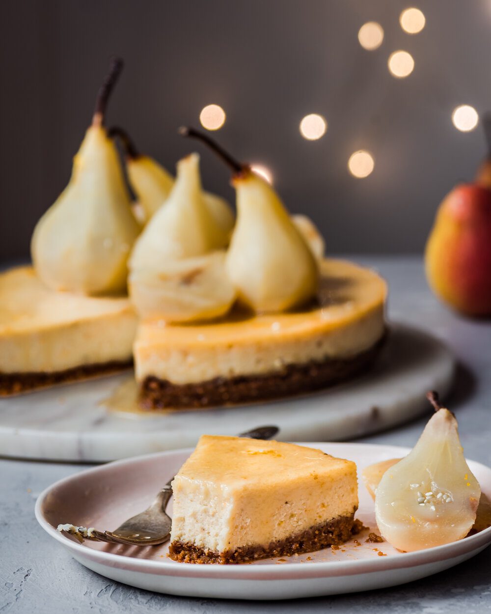 Piece of cheesecake and two poached pear halves on a plate with a fork.