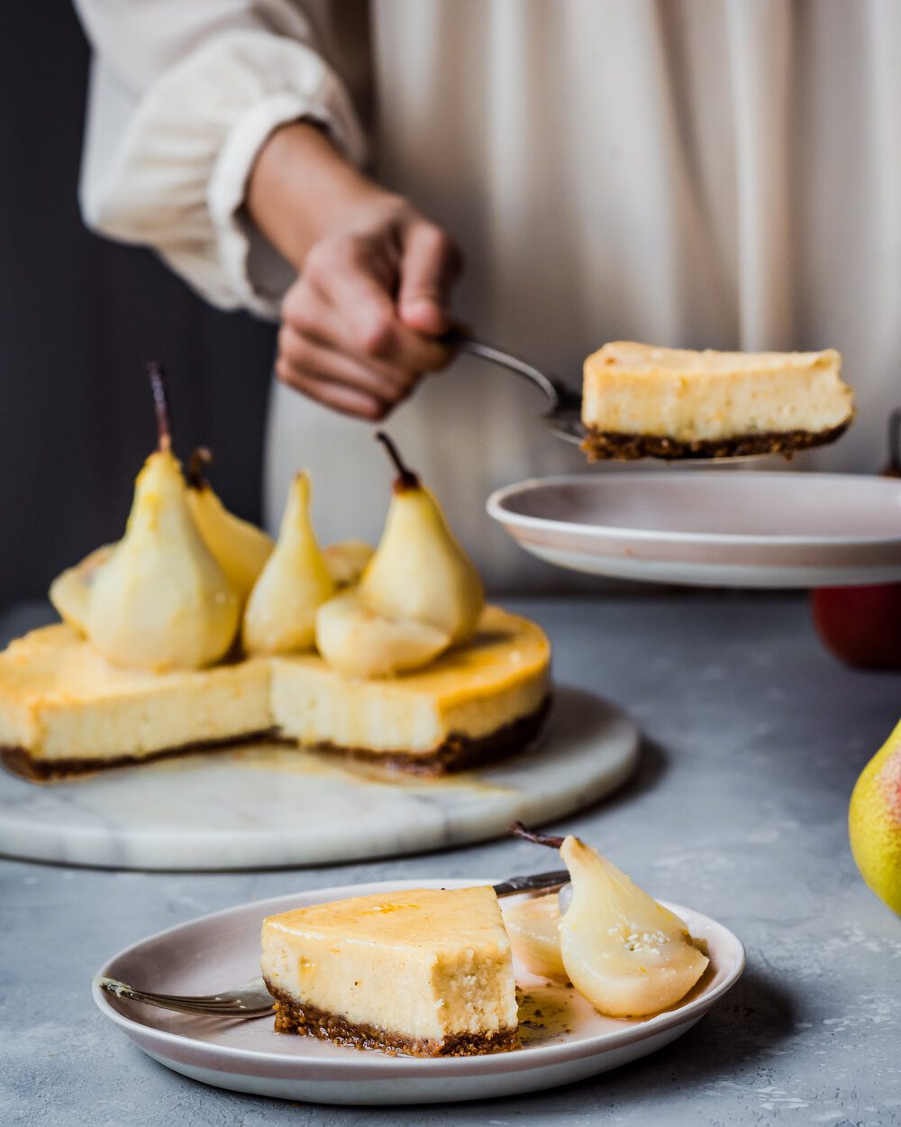 Woman placing piece of cheesecake on a plate next to full cheesecake.