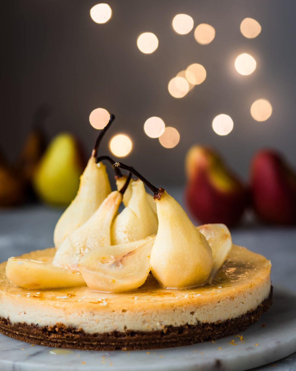 Poached pear halves on cheesecake on white marble board.