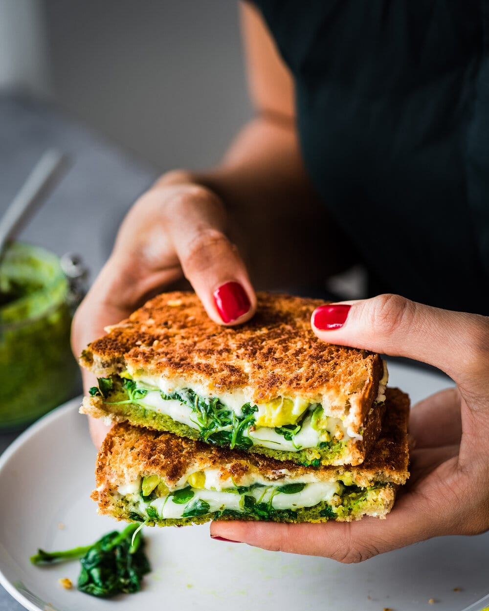 Woman holding halved Vegan Green Goddess Grilled Cheese over a plate.