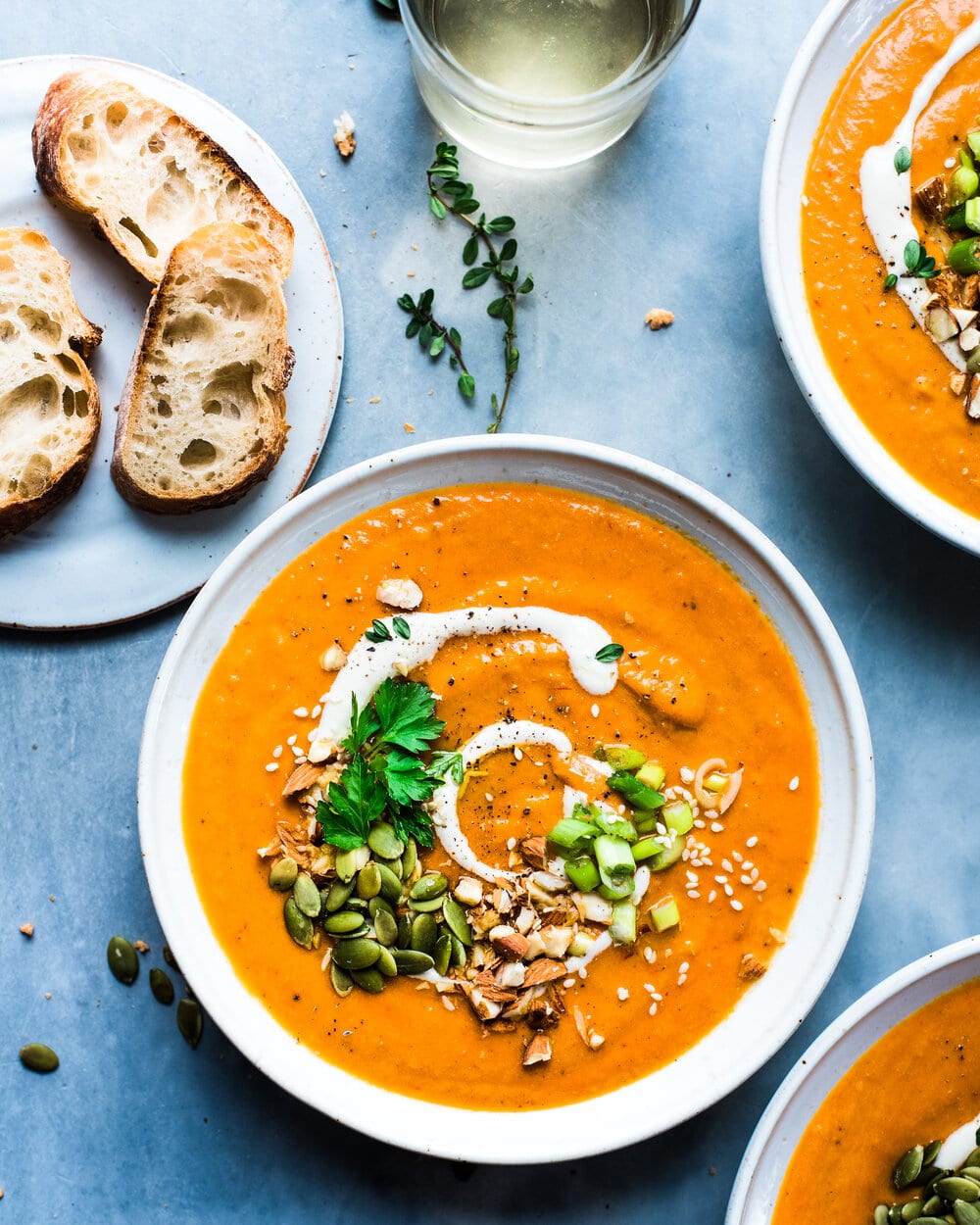 Three bowls of soup and a plate with bread slices on a grey table.