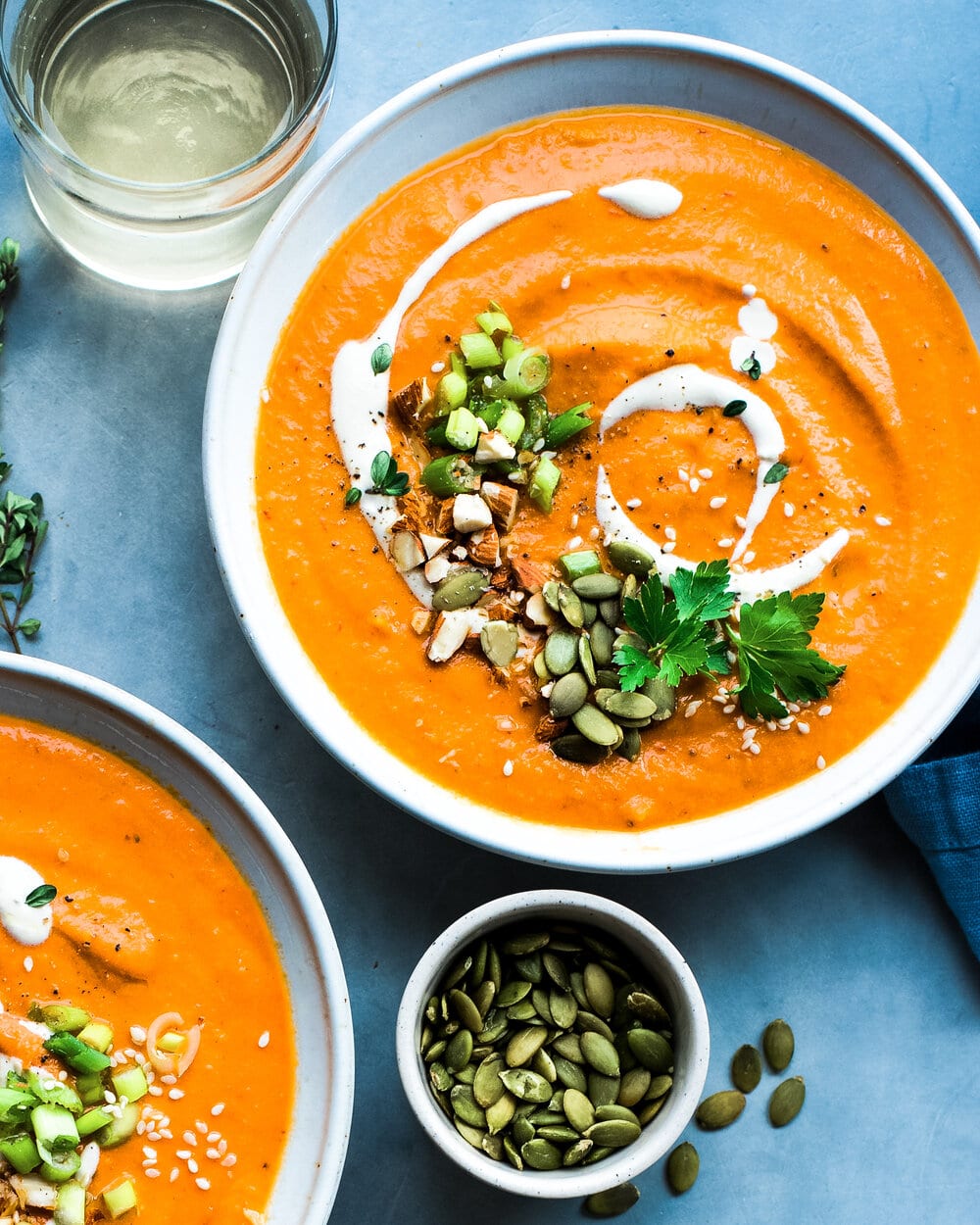 Close up of two bowls of soup and a small bowl of pumpkin seeds on a grey counter.