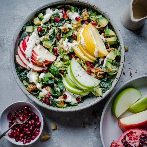Kale salad with sliced apples and pomegranates in a white bowl.