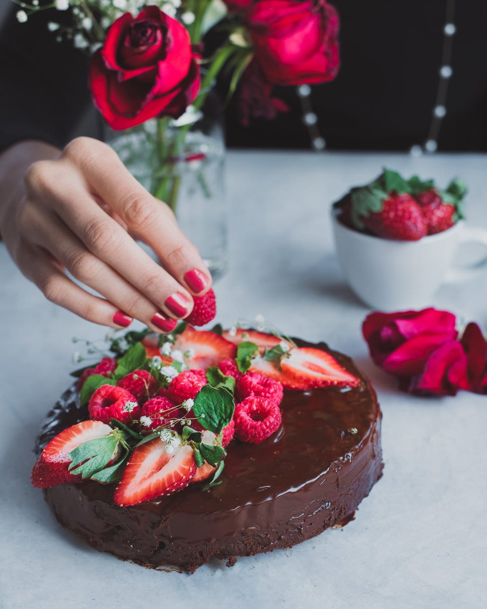 Woman placing berries all over chocolate cake on a white table.