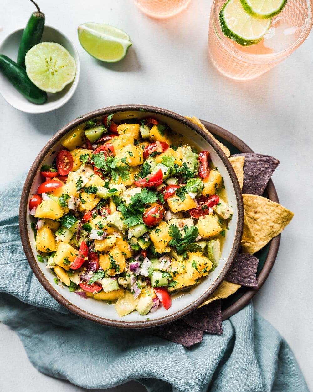 Mango and avocado salsa in a bowl with tortilla chips and limes.