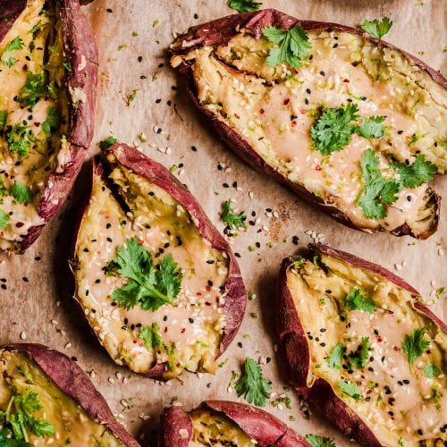 Baked sweet potatoes split open with tahini butter and sesame seeds inside