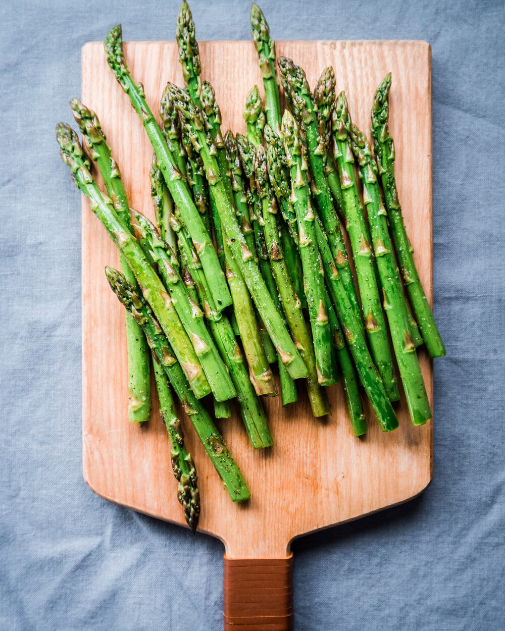 Asparagus spears on a small wooden cutting board.
