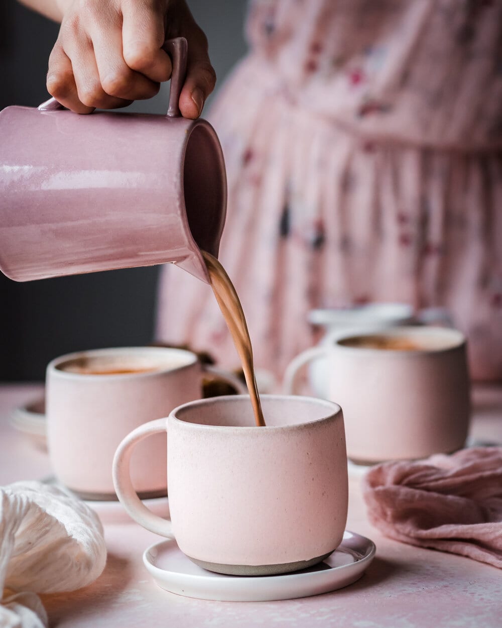 Woman pouring latte into a pink mug on a pink table.