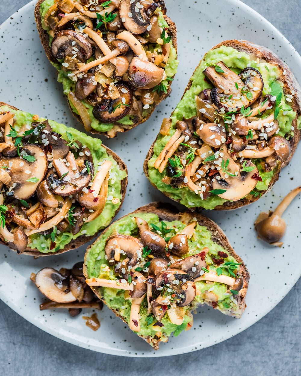 Four pieces of mushroom avocado toast on a white speckled plate.