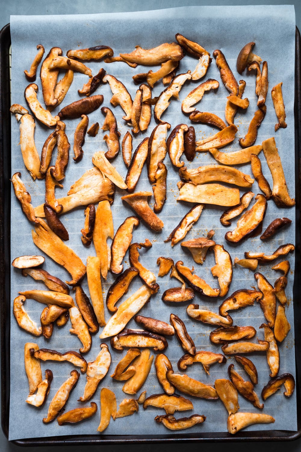 Thinly sliced marinated mushrooms on a piece of parchment paper on baking tray.