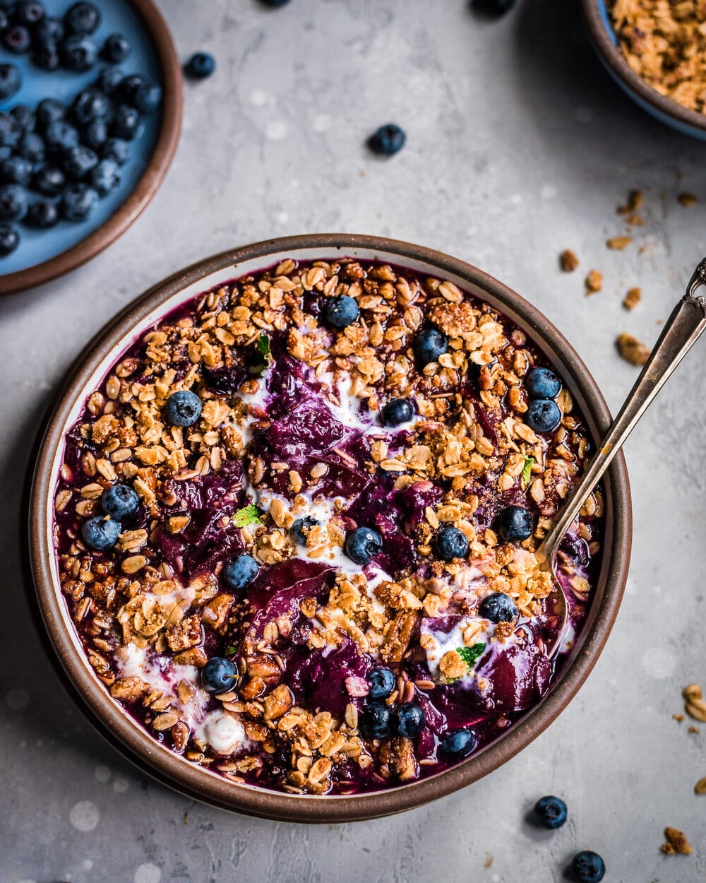 Overhead view of ice cream mixed into berry crisp in a bowl on a grey table.