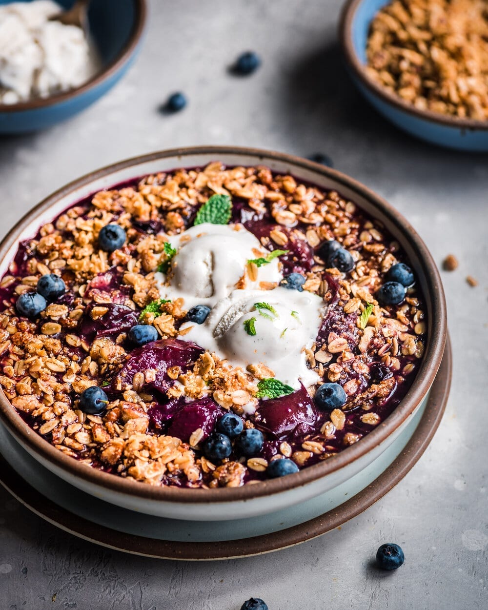 Berry Crisp in a bowl with vanilla ice cream on a grey table.