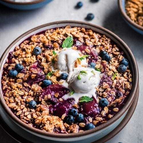 Berry crisp in bowl with ice cream on a grey table.