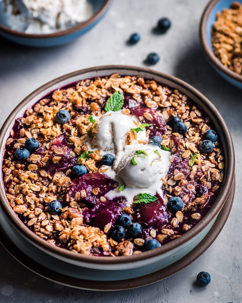 Berry crisp in bowl with ice cream on a grey table.