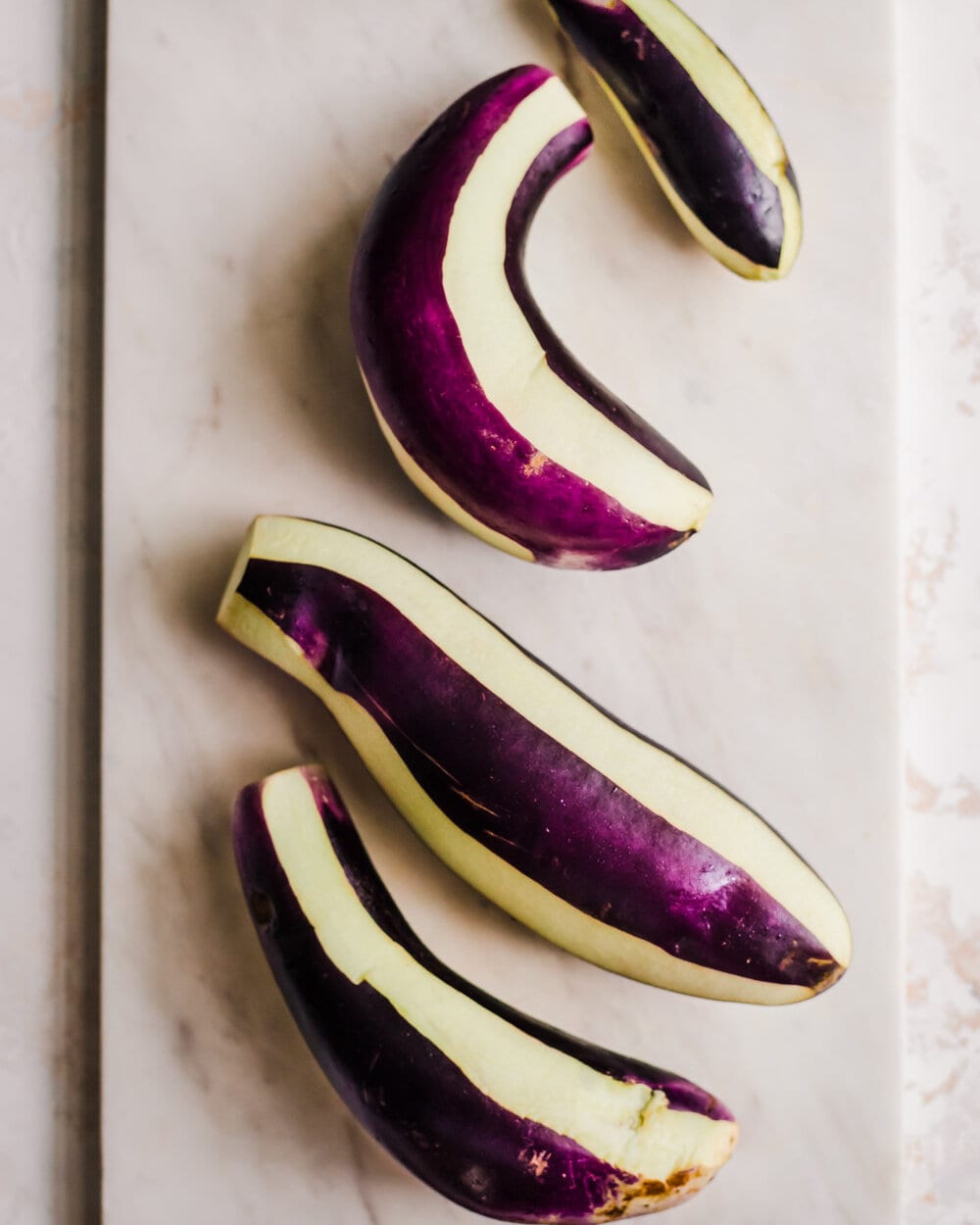eggplants partially peeled in an alternating zebra pattern on a white cutting board. 