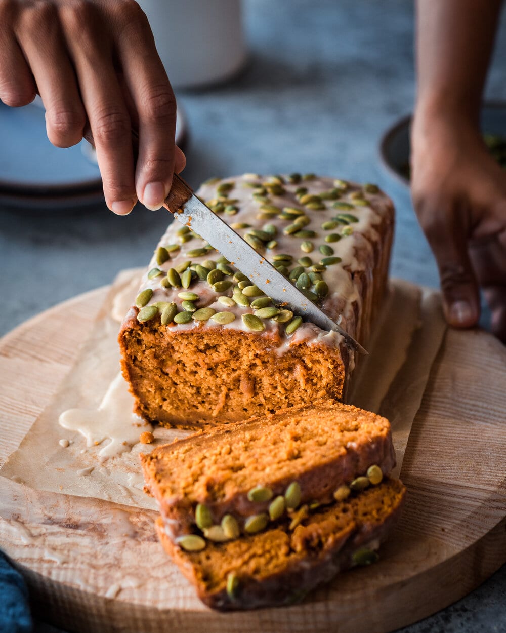 woman's hands slicing vegan pumpkin bread on cutting board
