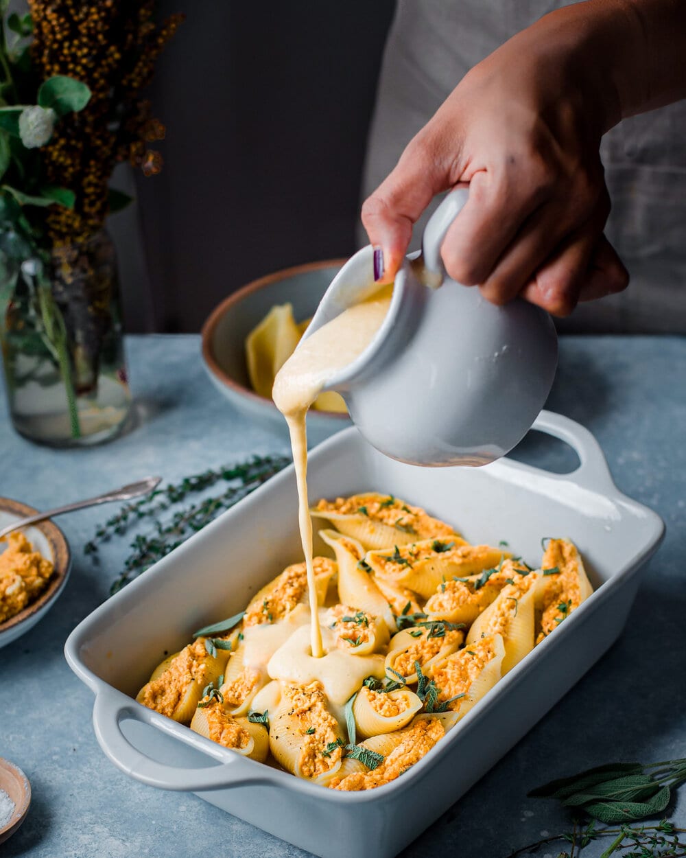 Vegan Pumpkin Ricotta Stuffed Shells. pouring garlic bechamel sauce on stuffed shells.