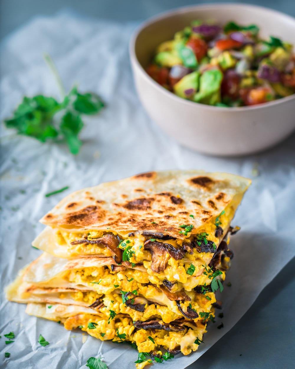 Four quartered quesadilla slices stacked on each other on a piece of parchment paper.