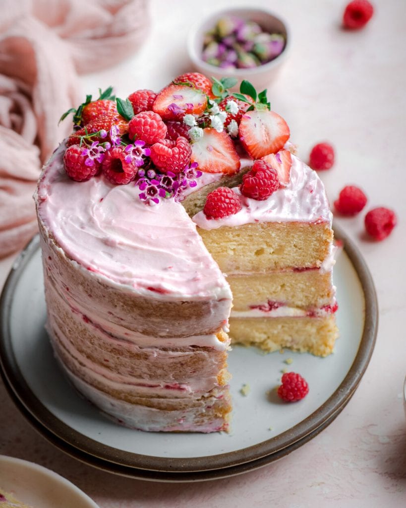 raspberry vanilla layer cake on plate with berry topping