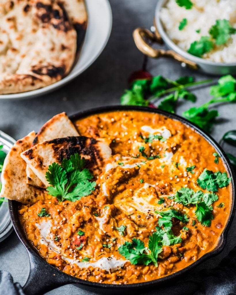 close-up shot of red lentil curry with naan and rice in background