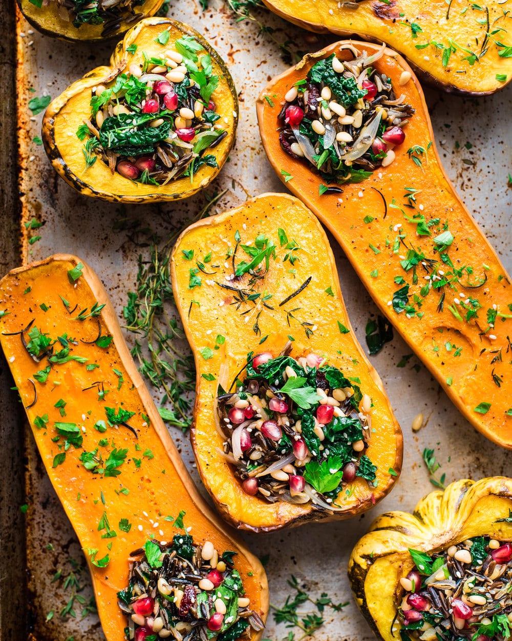Seven stuffed squash halves topped with fresh herbs on a baking tray.