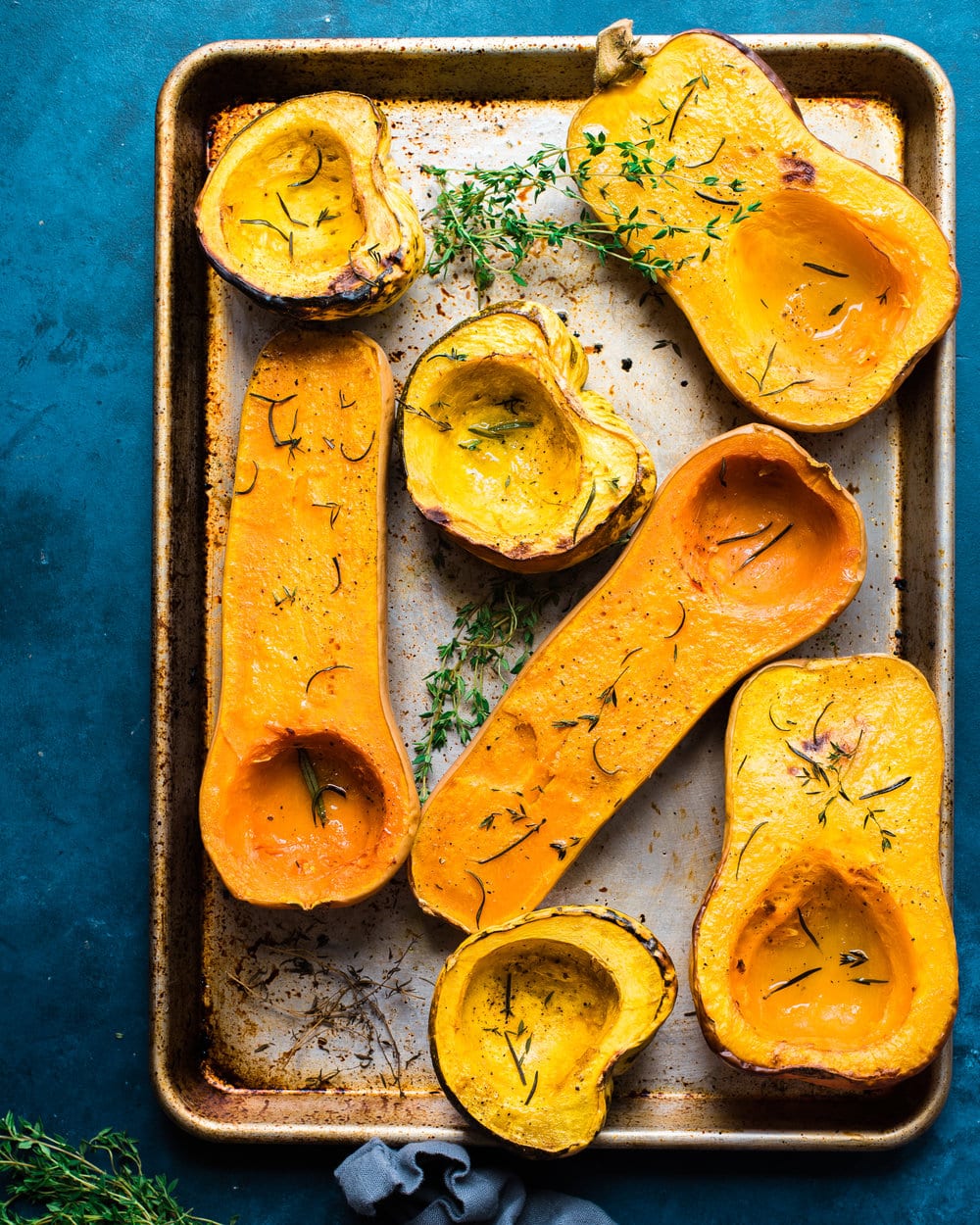 Seven roasted squash halves on a baking sheet on a blue table.