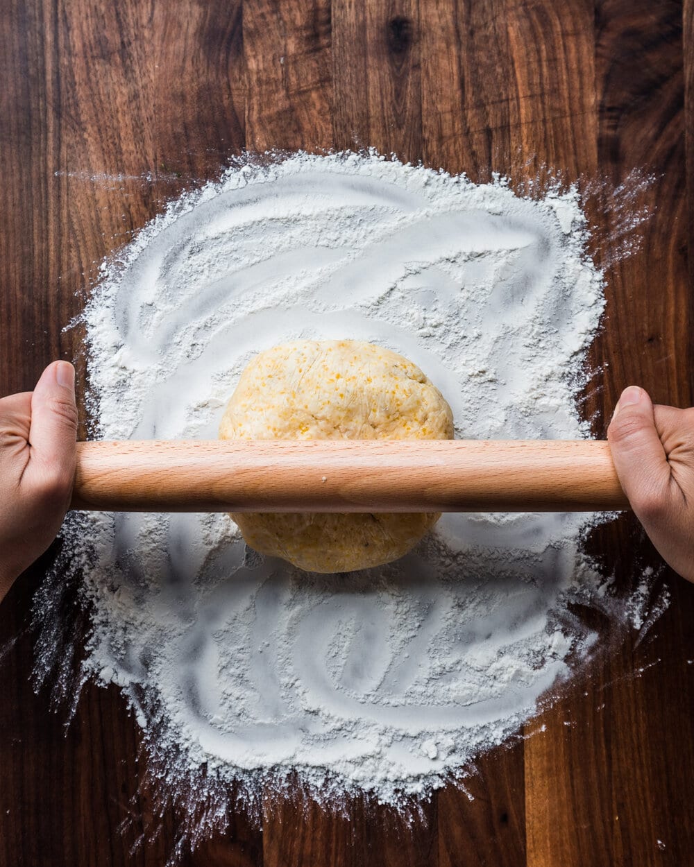 Person using rolling pin on a ball of dough on a floured work suface.