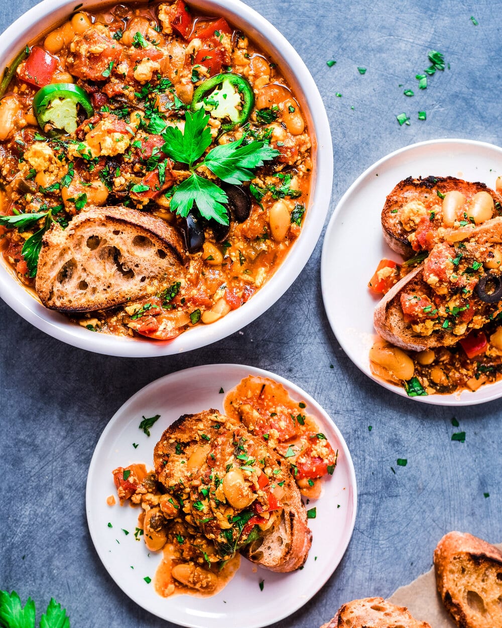 Two plates of shakshuka on toast next to one large serving plate.