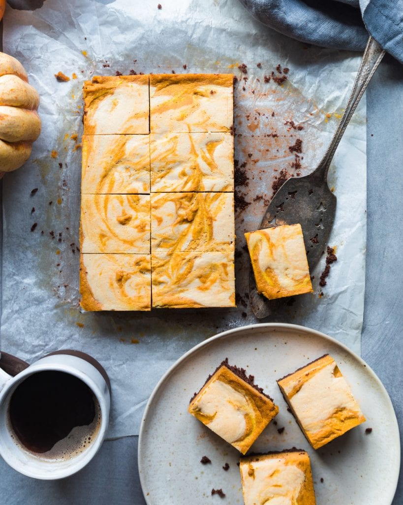 Plate of cheesecake bars next to the rest of the cheesecake on parchment paper.