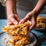 moody close up shot of buffalo chickpea quesadillas on a plate being picked up by woman's hands