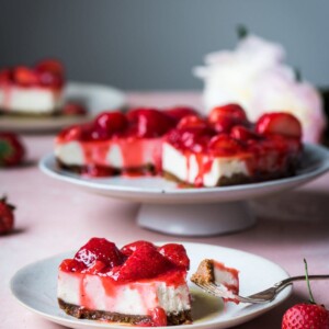 Vegan cheesecake slice covered in strawberry sauce on table.