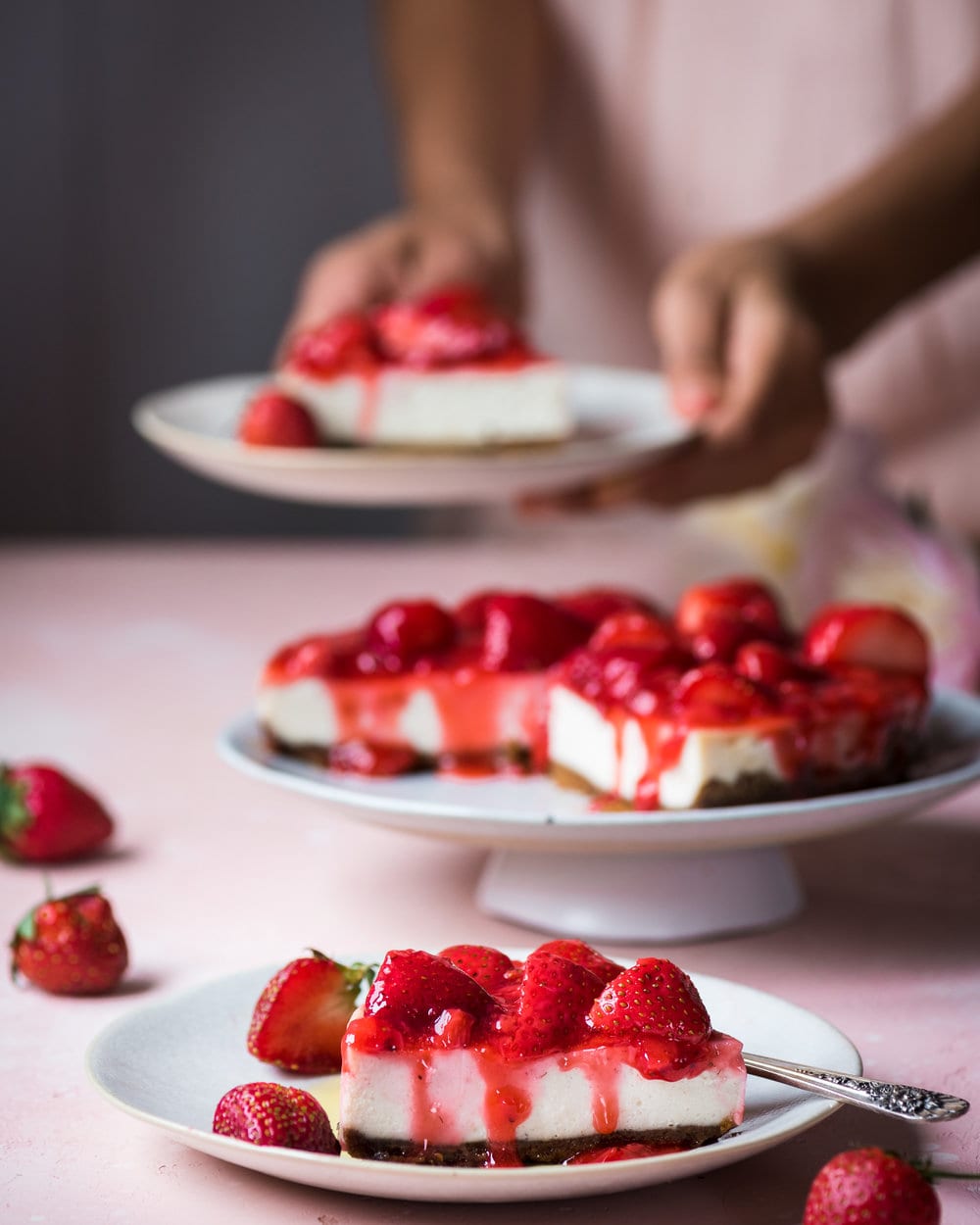 Woman holding slice of cheesecake above table with full cheesecake on it.