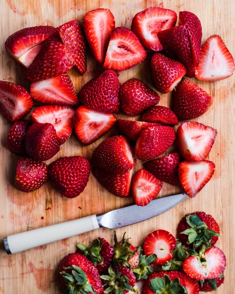 Halved strawberries, cut strawberry tops and a knife on a cutting board.