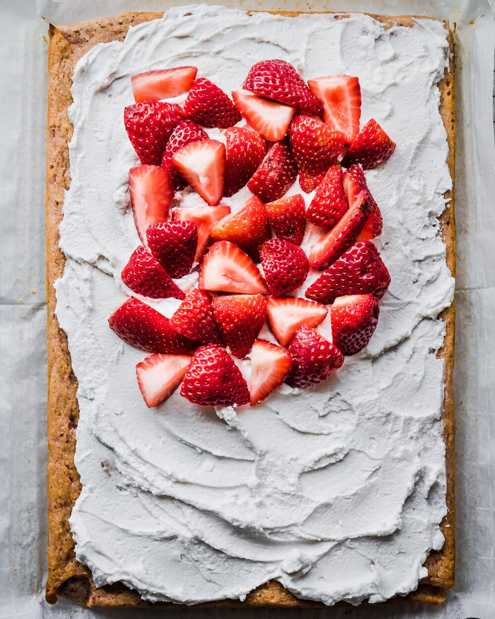 About half of the frosted sheet cake covered with sliced strawberries.