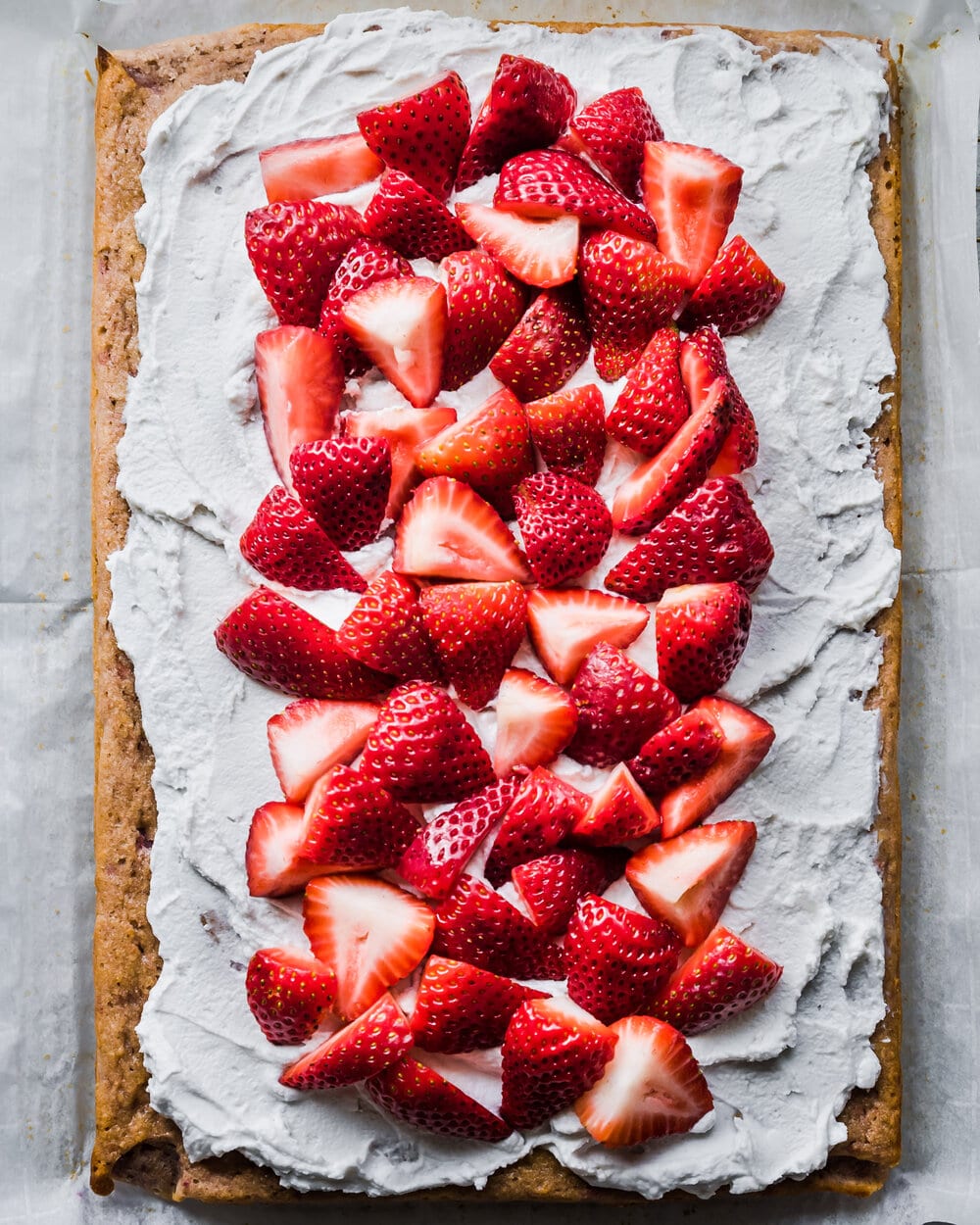 About three fourths of the frosted sheet cake covered with sliced strawberries.