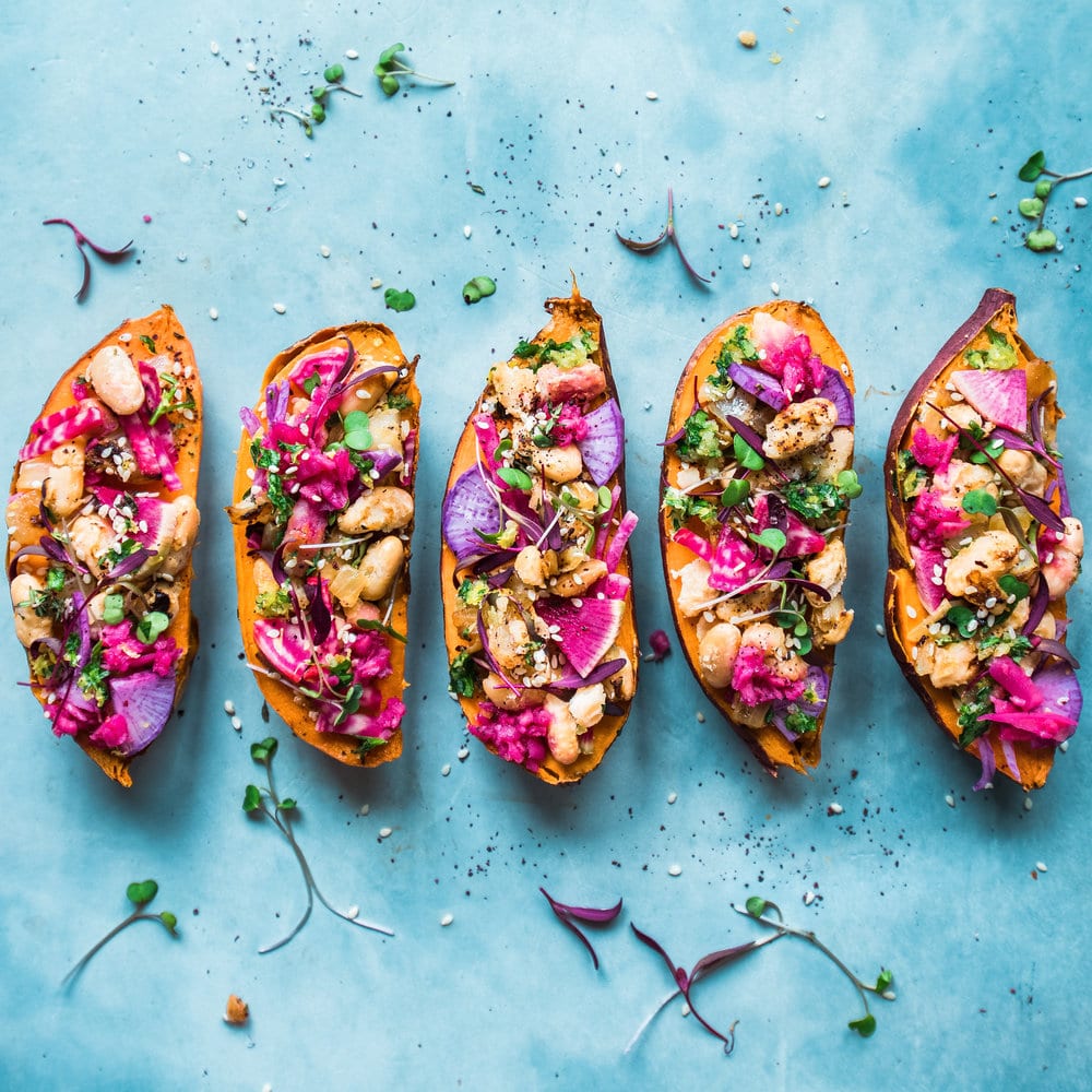 Five stuffed sweet potatoes lined up on a blue table.