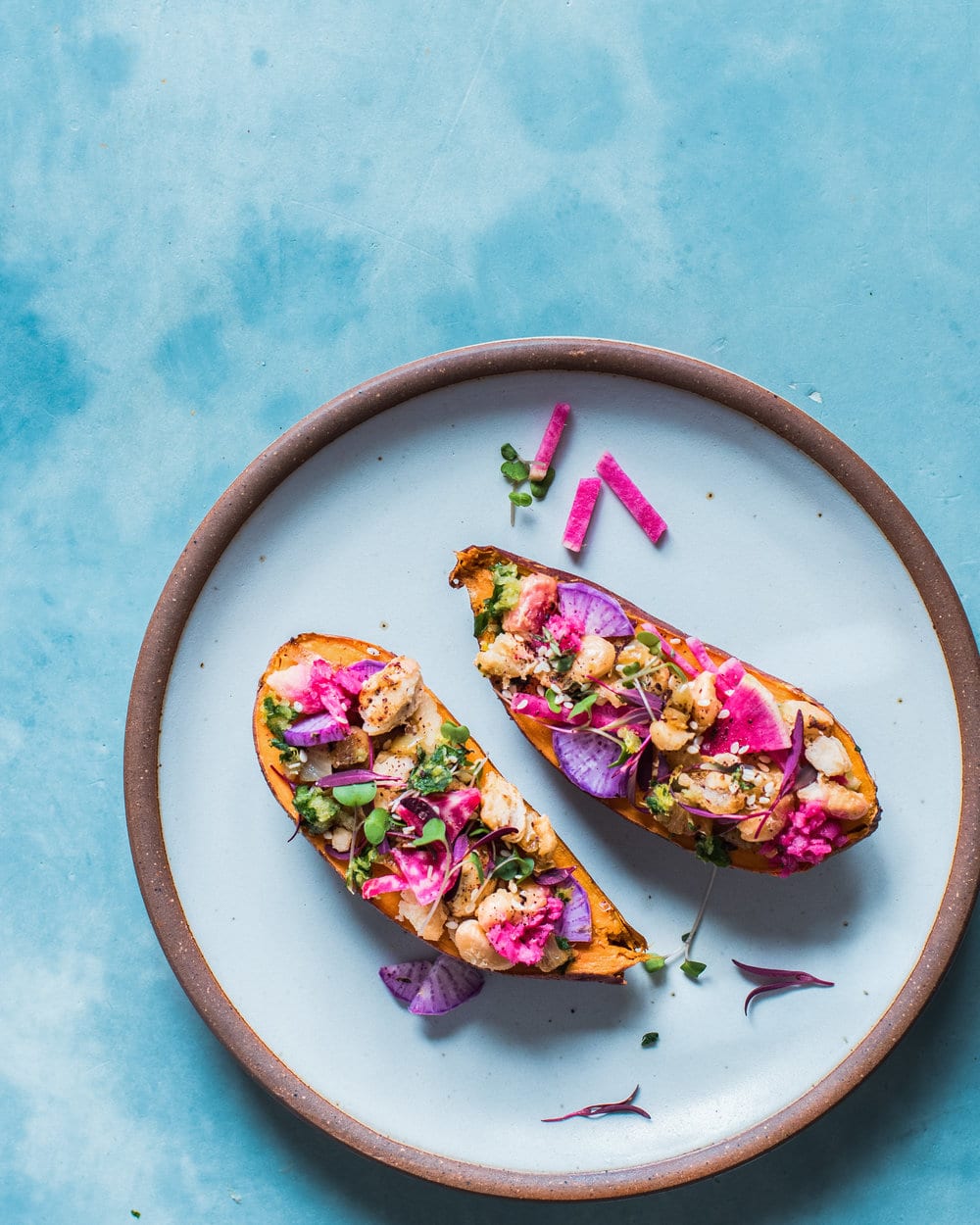 Two halves of a stuffed sweet potato on a blue plate on a blue table.