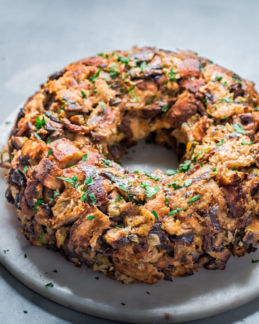 Side view of backlit vegan mushroom stuffing wreath on a round marble serving board.