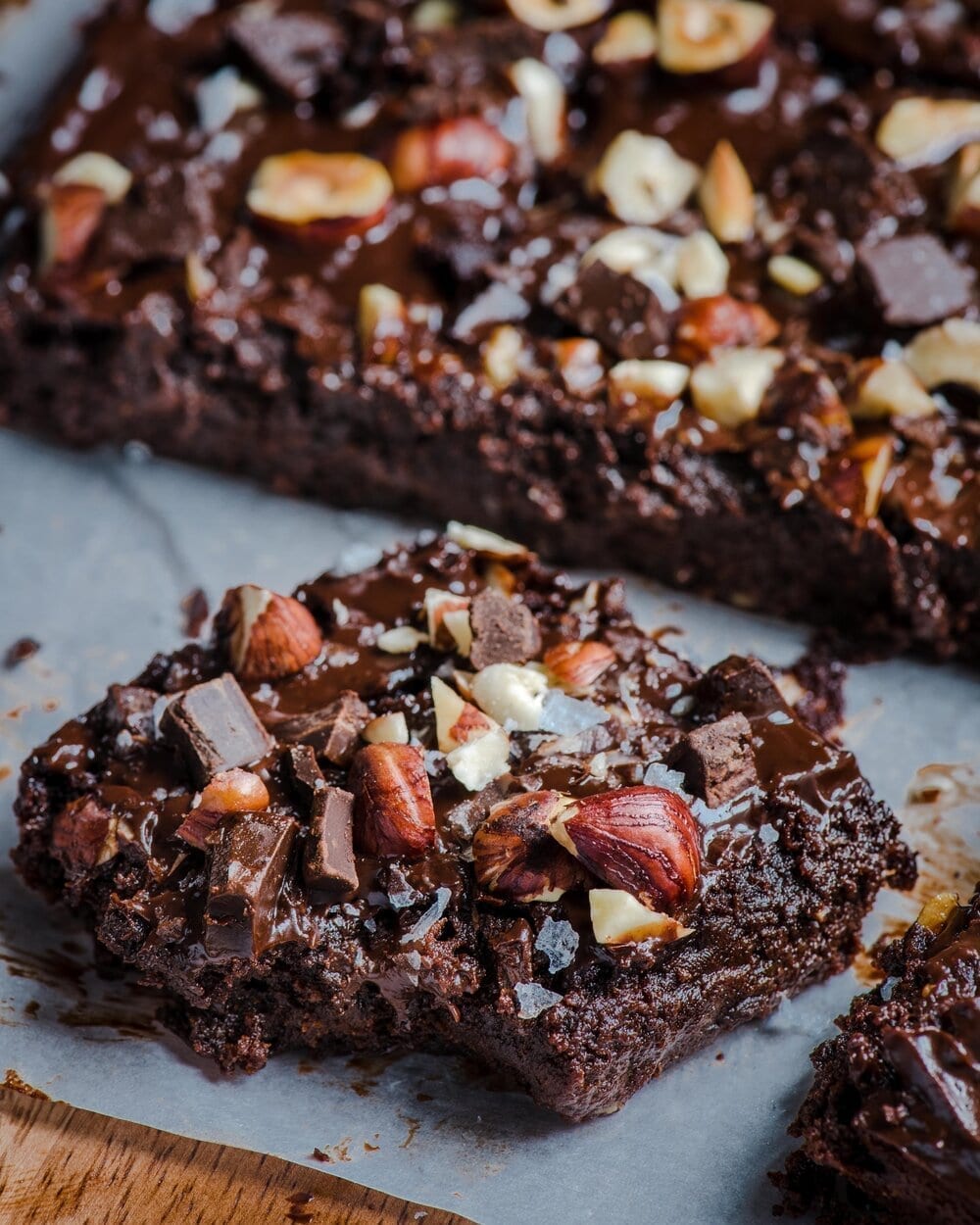 An individual brownie on a piece of parchment paper in front of the rest of the brownies.