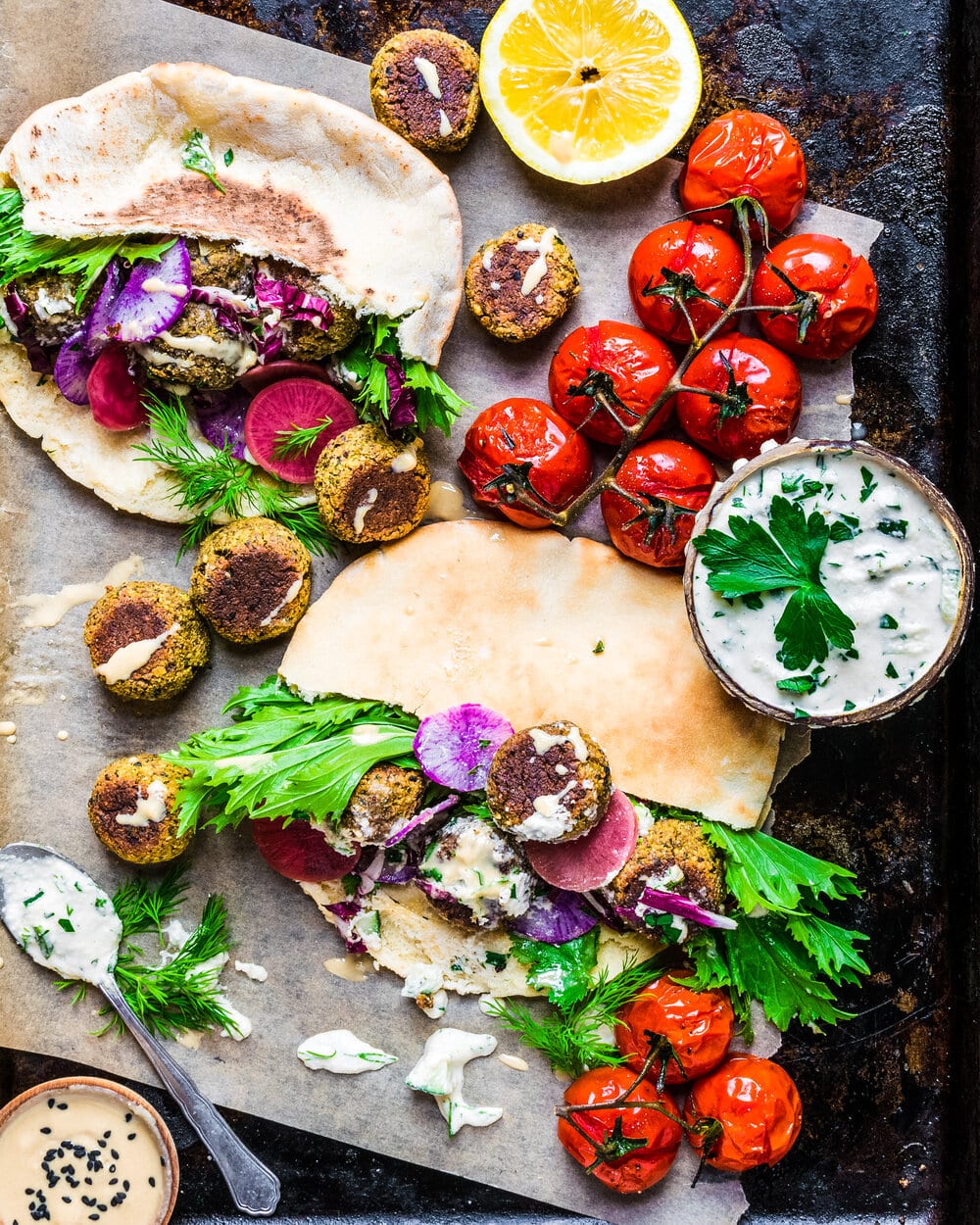 Falafel, tomatoes, pita bread, tzatziki and herbs on parchment paper.