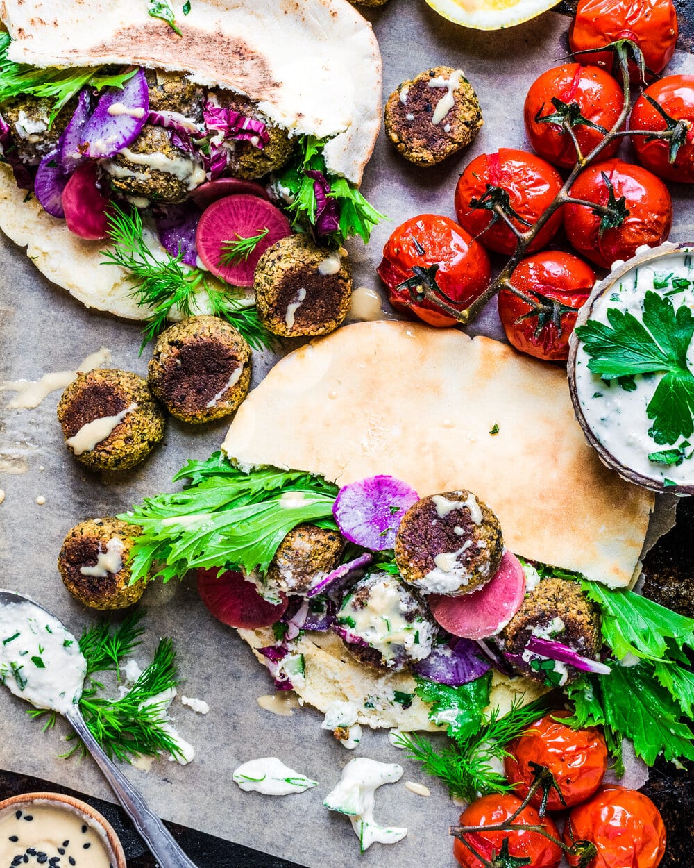 Pitas with falafel, veggies and herbs on a piece of parchment paper.