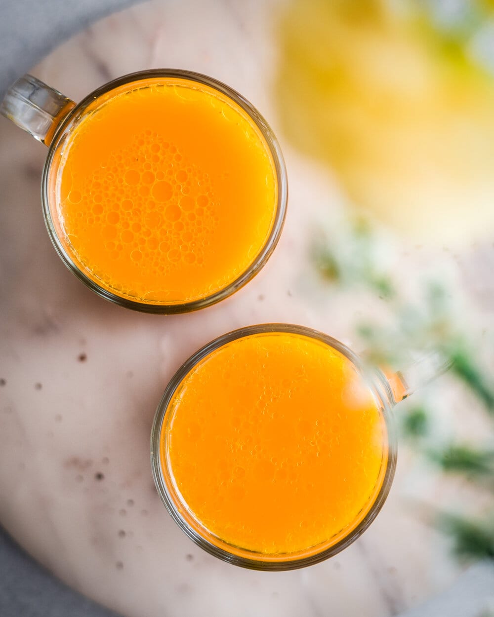 Two glass mugs filled with turmeric tonic on a marble serving tray.