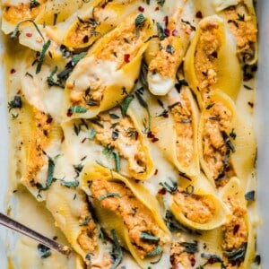 close up of pumpkin ricotta stuffed shells in a large baking dish.