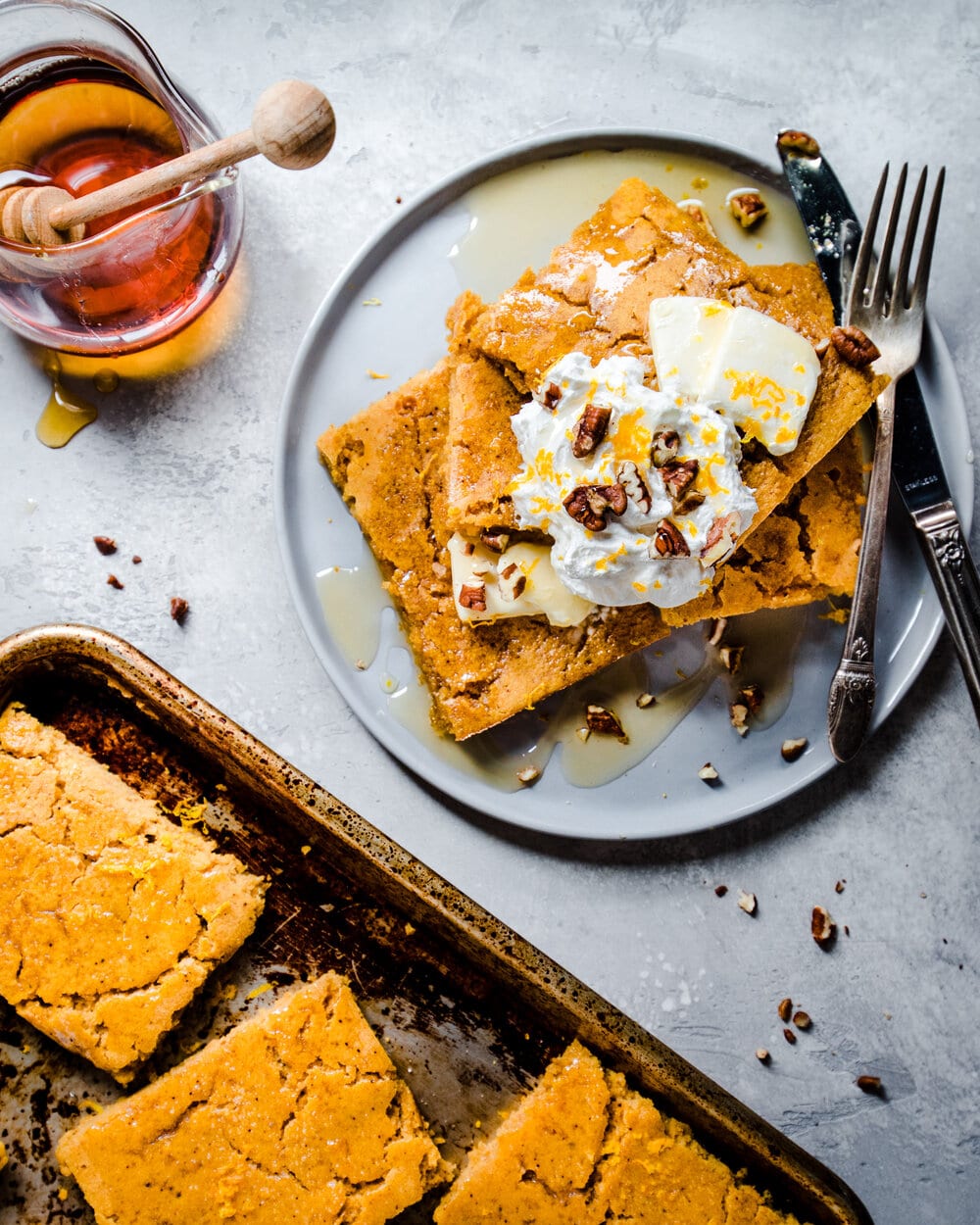 Stack of three sheet pancakes with butter, whipped cream and orange zest on a plate with utensils.